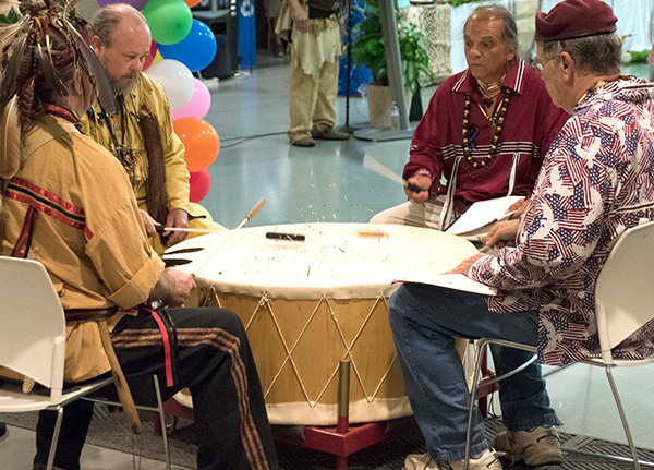Four men sit and beat large drum